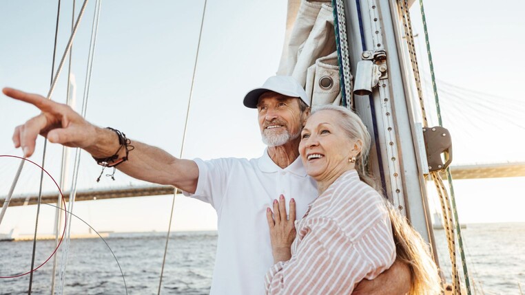 Ein älteres Paar auf einem Segelboot. Der Mann deutet in die Ferne.