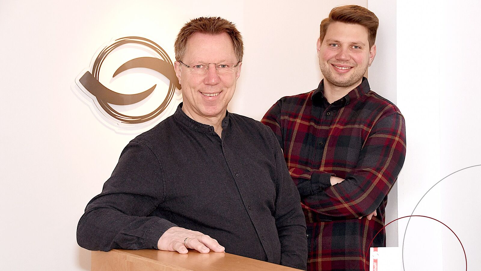 Jens-Peter Markhoff und sein Sohn Lasse stehen in ihren Praxisräumen und lächeln in die Kamera.